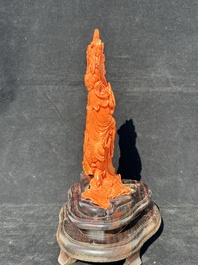 A Chinese red coral Guanyin holding a lotus on wooden stand, 19/20th C.