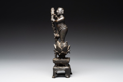 A Chinese bronze incense holder of a boy standing on a lotus, Ming