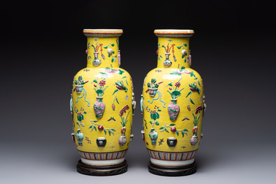 A pair of Chinese famille rose yellow-ground relief-decorated vases with wooden stands, 19th C.