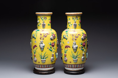 A pair of Chinese famille rose yellow-ground relief-decorated vases with wooden stands, 19th C.