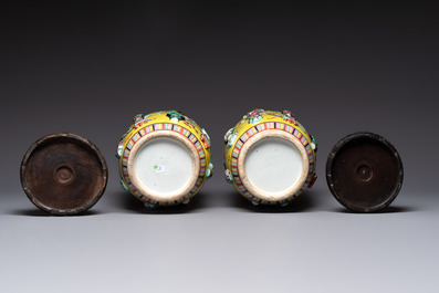 A pair of Chinese famille rose yellow-ground relief-decorated vases with wooden stands, 19th C.