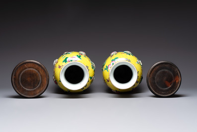 A pair of Chinese famille rose yellow-ground relief-decorated vases with wooden stands, 19th C.