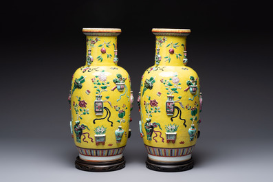 A pair of Chinese famille rose yellow-ground relief-decorated vases with wooden stands, 19th C.
