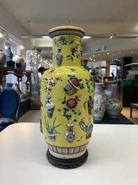 A pair of Chinese famille rose yellow-ground relief-decorated vases with wooden stands, 19th C.