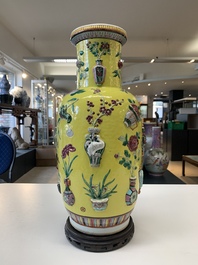A pair of Chinese famille rose yellow-ground relief-decorated vases with wooden stands, 19th C.