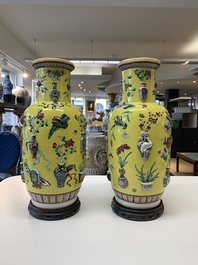 A pair of Chinese famille rose yellow-ground relief-decorated vases with wooden stands, 19th C.