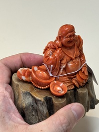 A Chinese red coral sculpture of a Milefo Buddha on wooden stand, 19/20th C.