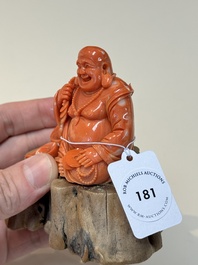 A Chinese red coral sculpture of a Milefo Buddha on wooden stand, 19/20th C.
