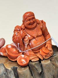 A Chinese red coral sculpture of a Milefo Buddha on wooden stand, 19/20th C.