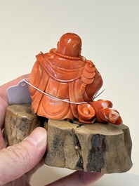 A Chinese red coral sculpture of a Milefo Buddha on wooden stand, 19/20th C.