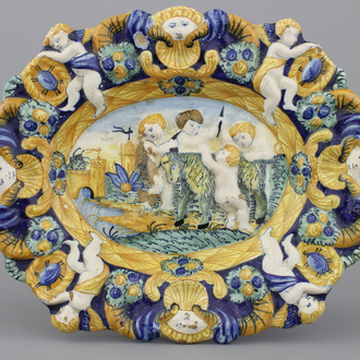 A relief-moulded polychrome oval dish with putti dehorning a goat, 18/19th C.