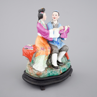 A Chinese porcelain model of an amorous couple, on wooden stand, 20th C.