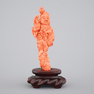 A Chinese carved red coral figure on a wooden stand, 19/20th C.