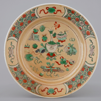 A Chinese famille verte café au lait ground plate with precious objects, Kangxi