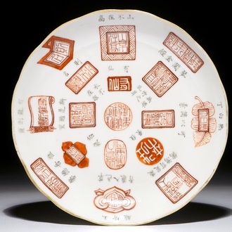 Une assiette en porcelaine de Chine à décor de calligraphie et marques en rouge de fer et noir, 19/20ème
