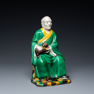 A Chinese verte biscuit figure of a Luohan holding a dog, probably Qing