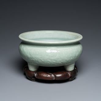 A Chinese celadon-glazed tripod censer with floral scrolls on wooden stand, Qing