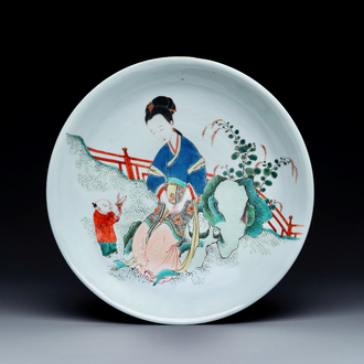 A Chinese famille verte dish with a lady in a garden and a boy offering her a 'jue' vessel, Kangxi