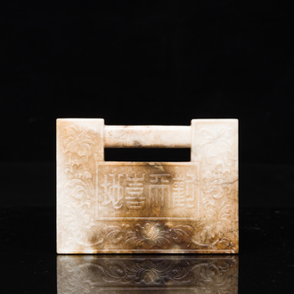 A Chinese white and russet jade lock-shaped plaque with inscription 'Huan Tian Xi Di 歡天喜地', Qing