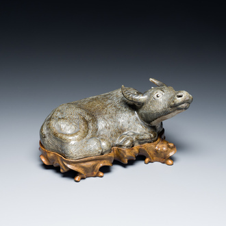 A Chinese brown-grey-glazed recumbent water buffalo on wooden stand, 19th C.