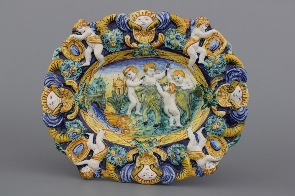 A relief-moulded polychrome oval dish with putti dehorning a goat, 18/19th C.