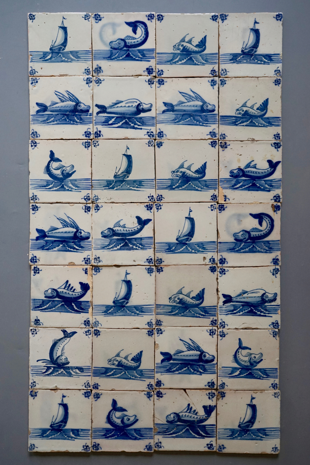 Een set van 28 blauw-witte Delftse tegels met maritieme voorstellingen uit het atelier Pulinckx, Brugge, 18e eeuw