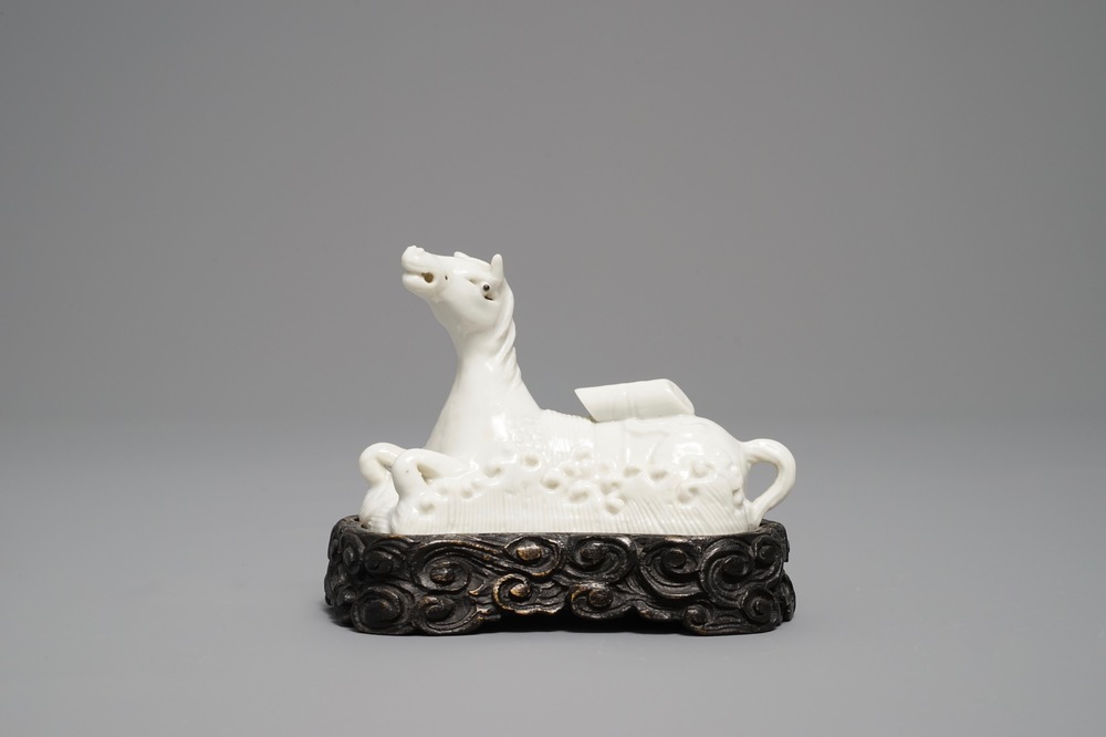 Een Chinees Dehua blanc de Chine model van een liggend paard op houten basis, Kangxi