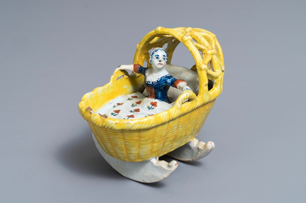 A polychrome Dutch Delft model of a girl in a cradle, 18th C.