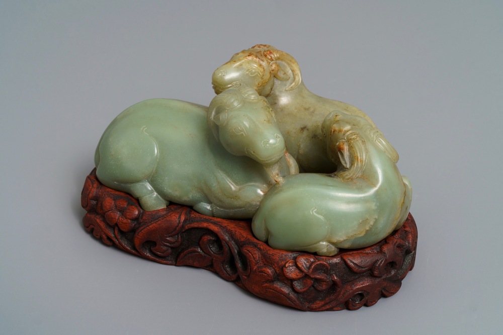 A Chinese pale celadon and russet jade 'three rams' group on carved wooden stand, 18/19th C.