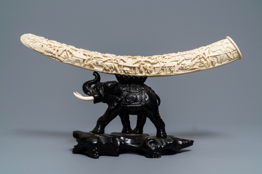 A Chinese carved ivory tusk on wooden elephant stand, ca. 1900
