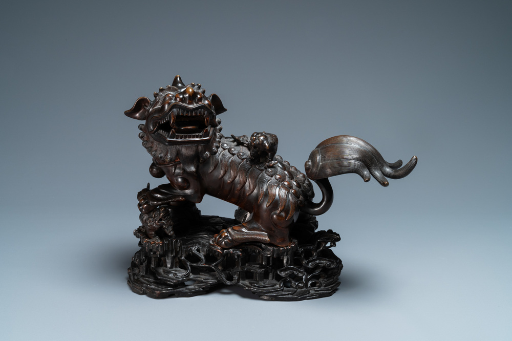 A Chinese bronze model of a Buddhist lion on a finely carved wooden stand, 18th C.