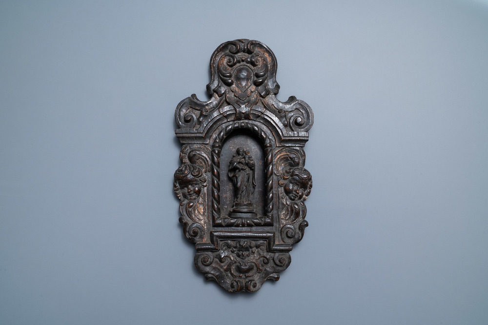 A patinated wooden niche with a Madonna with child flanked by cherub heads, 18th C.