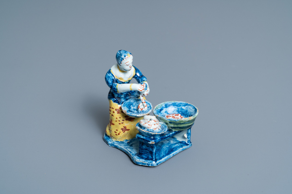 A rare polychrome Dutch Delft figure of a butcher's lady stuffing sausages, 18th C.