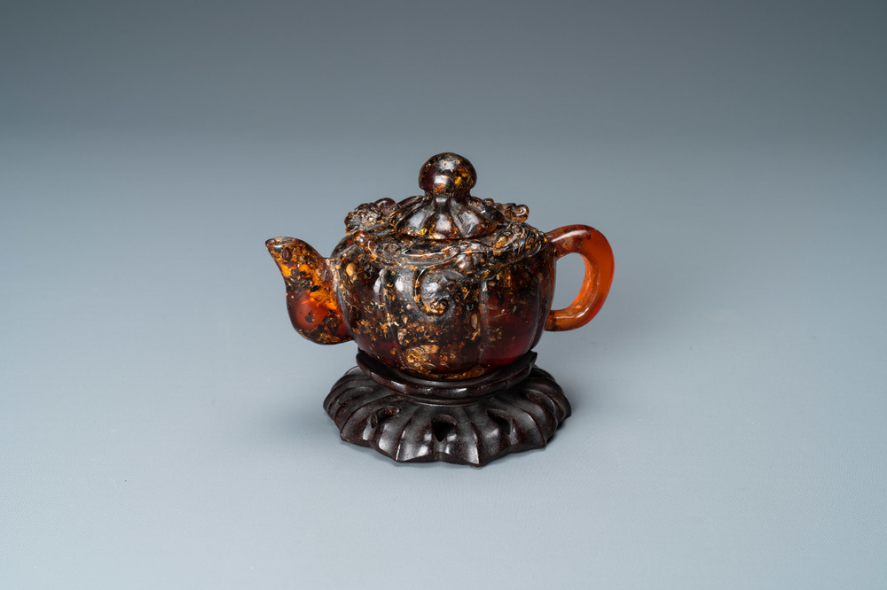 A Chinese carved amber teapot and cover on wooden 'lotus' stand, 19th C.