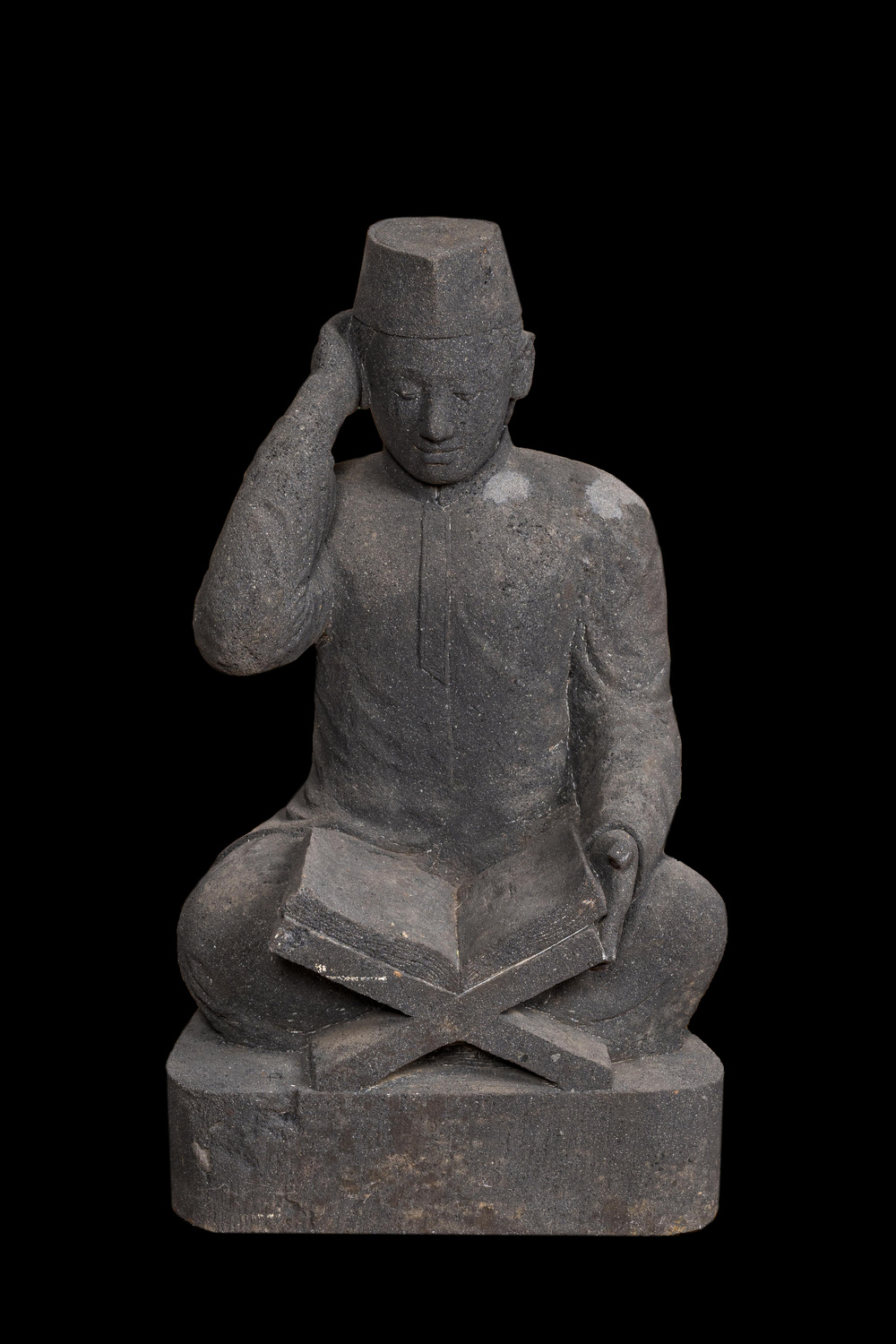 A basalt sculpture of a reading student, Indonesia, 20th C.