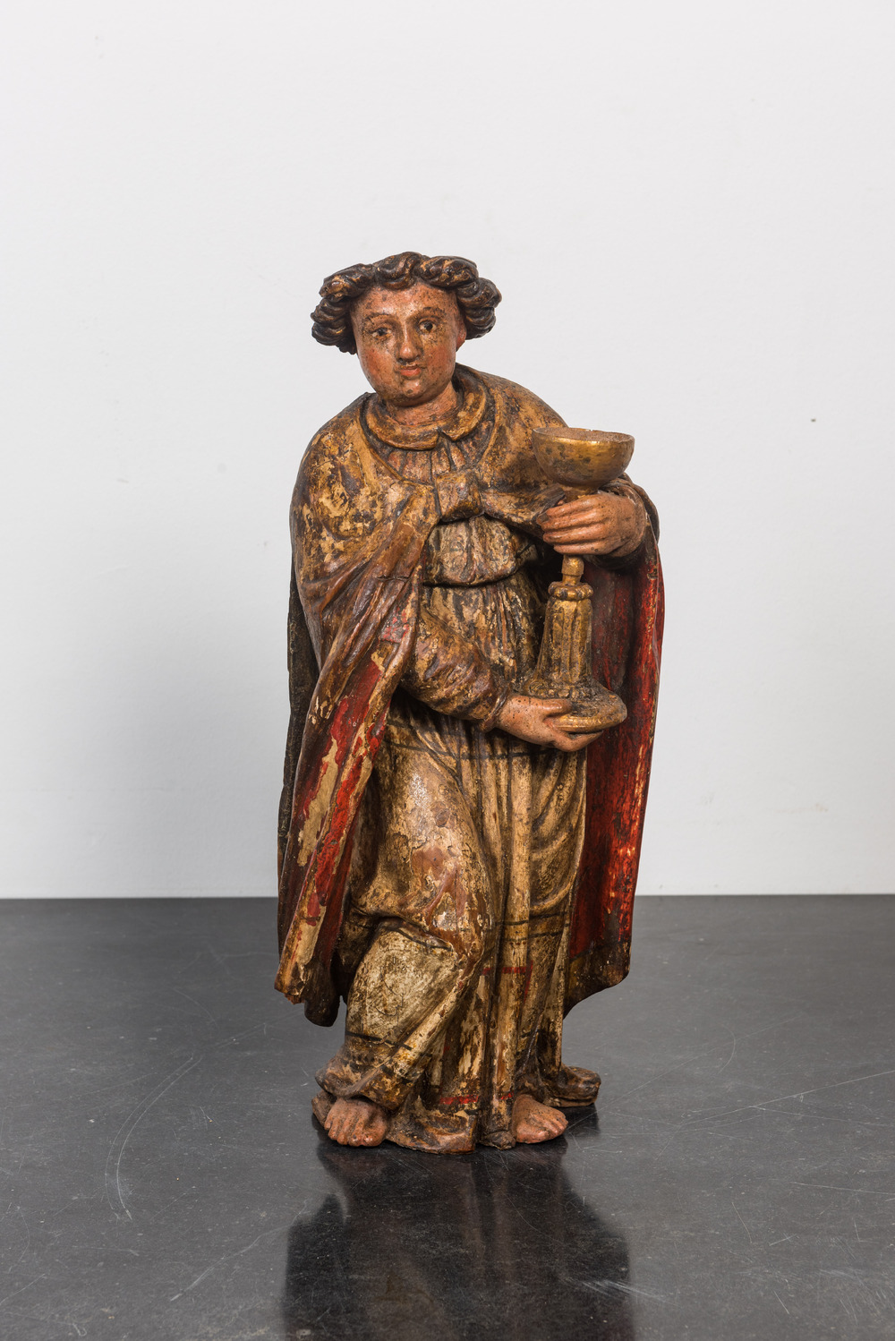 A polychrome wooden figure of John the apostle holding a chalice, 17th C.