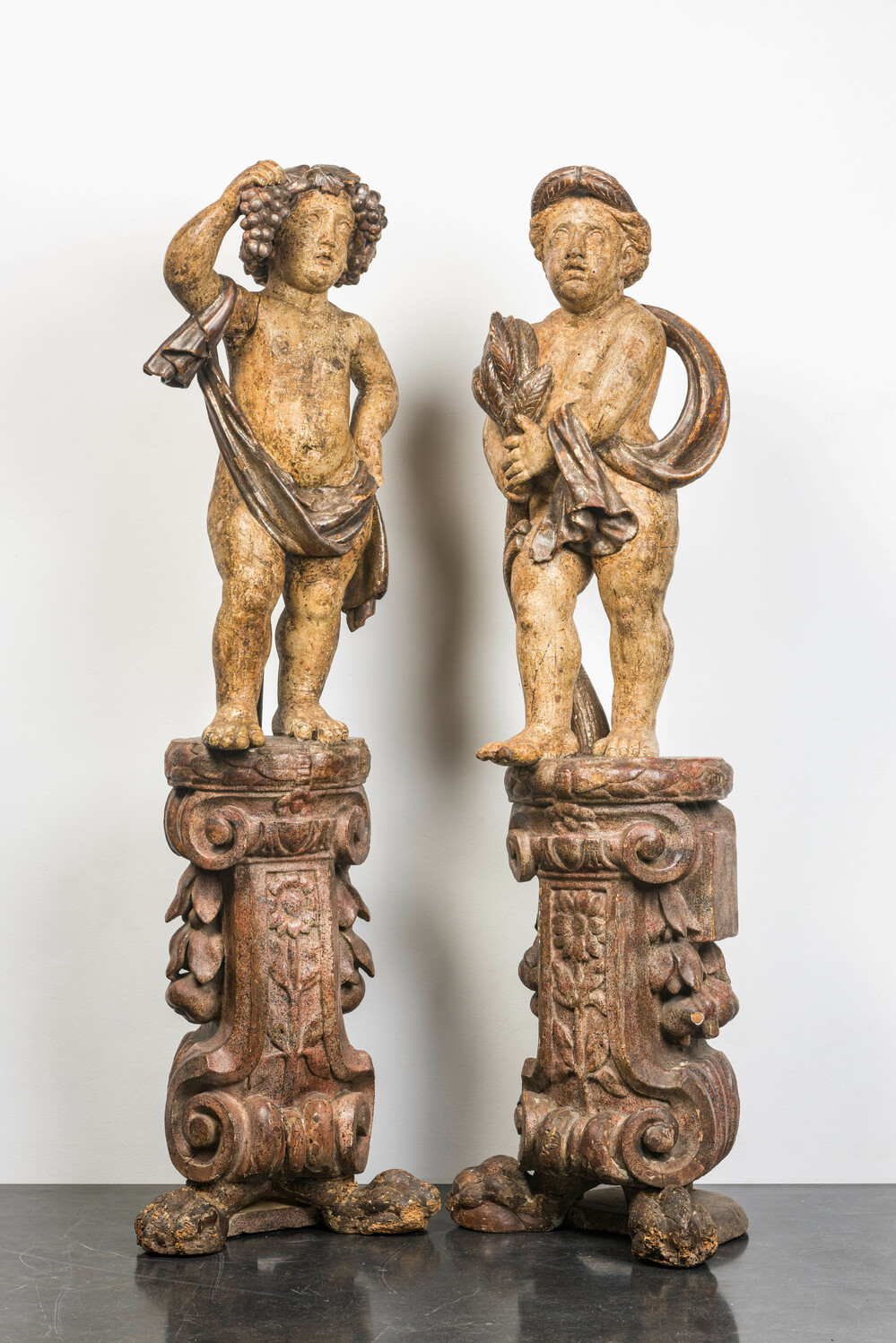 A pair of large polychrome wooden allegorical putti on bases, probably Italy, 18th C.