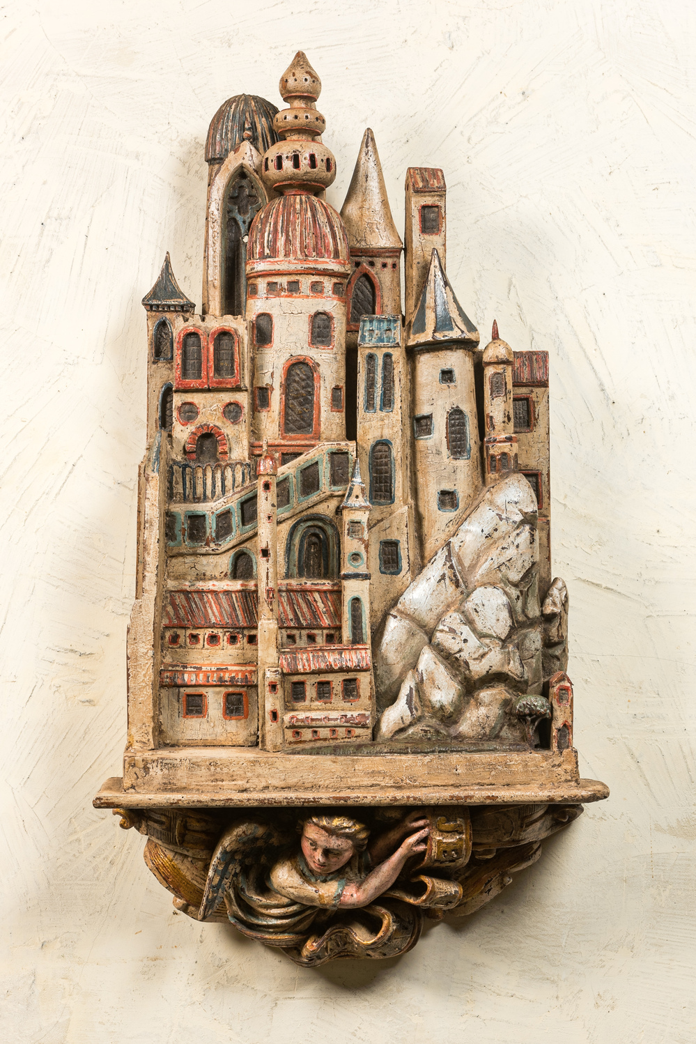 Een groot polychroom houten 'Jeruzalem' reli&euml;f op een console met gevleugelde putto, 19e eeuw