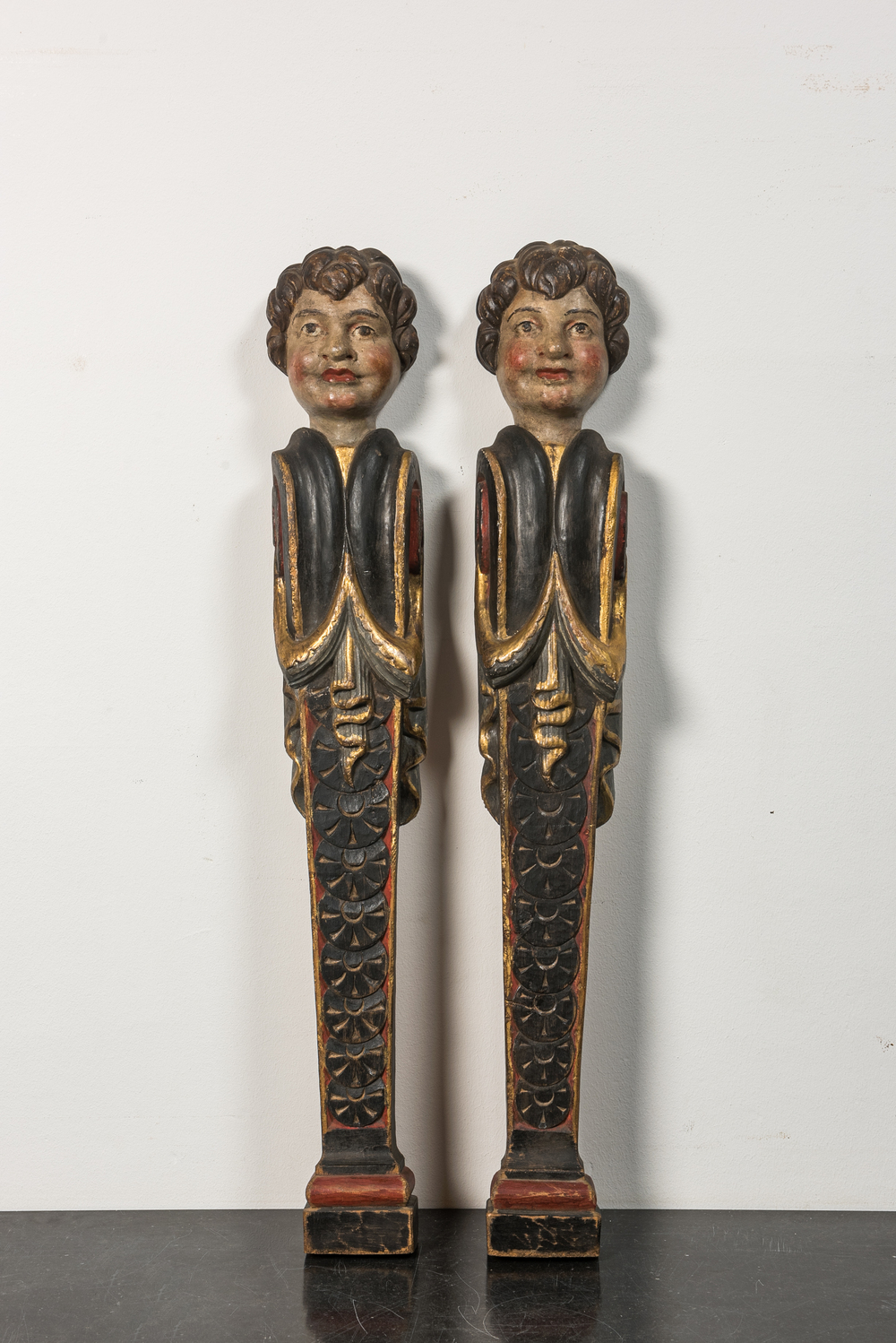 A pair of polychrome wooden pillars or atlants with boys' heads, 19th C.