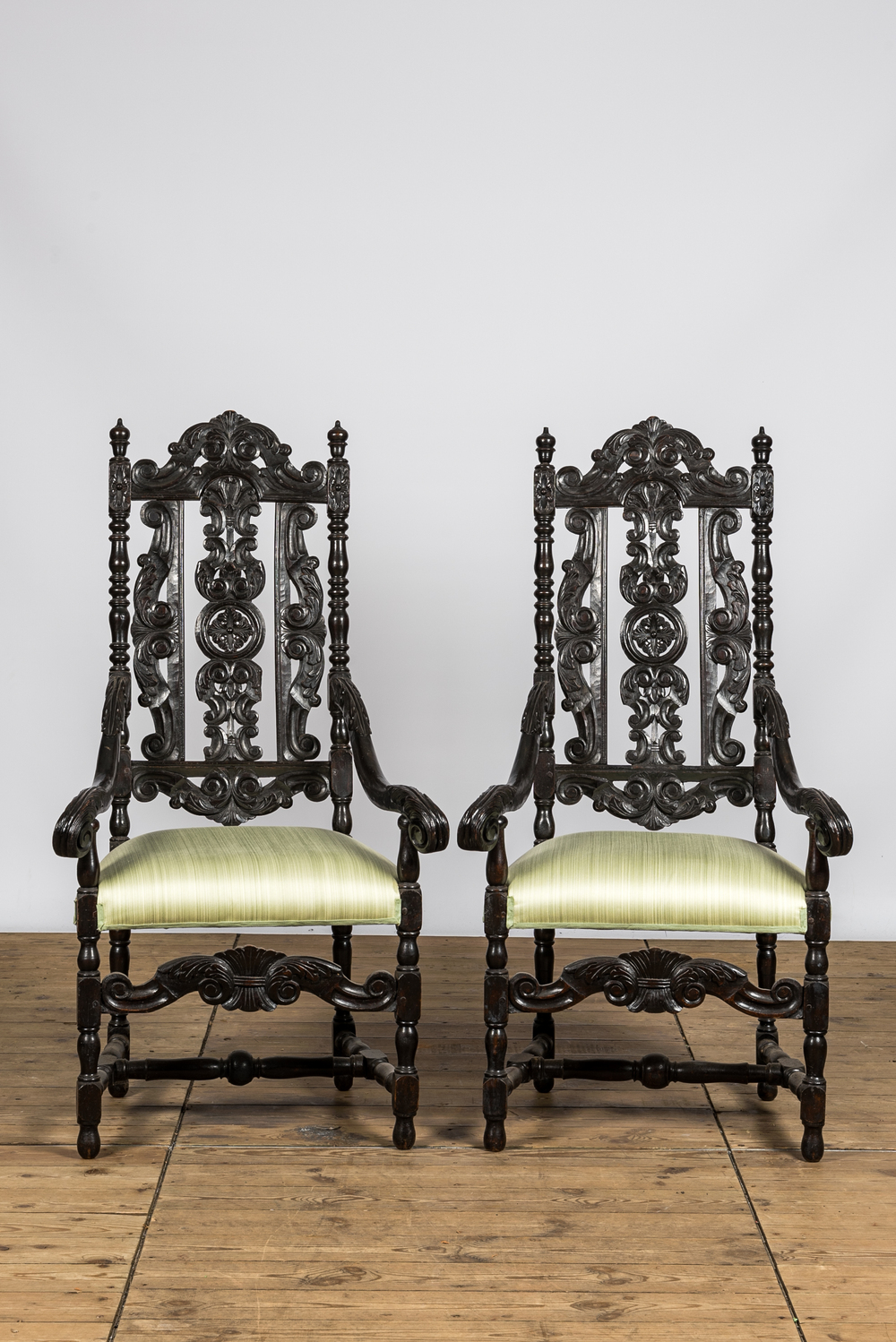 A pair of ebonised wooden armchairs with green silk upholstery, 19th C.