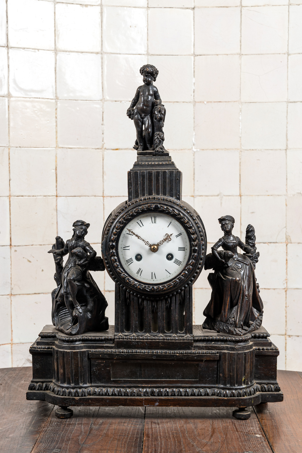 An ebonised mantel clock with romantic figures and topped with a putto, 19th C.