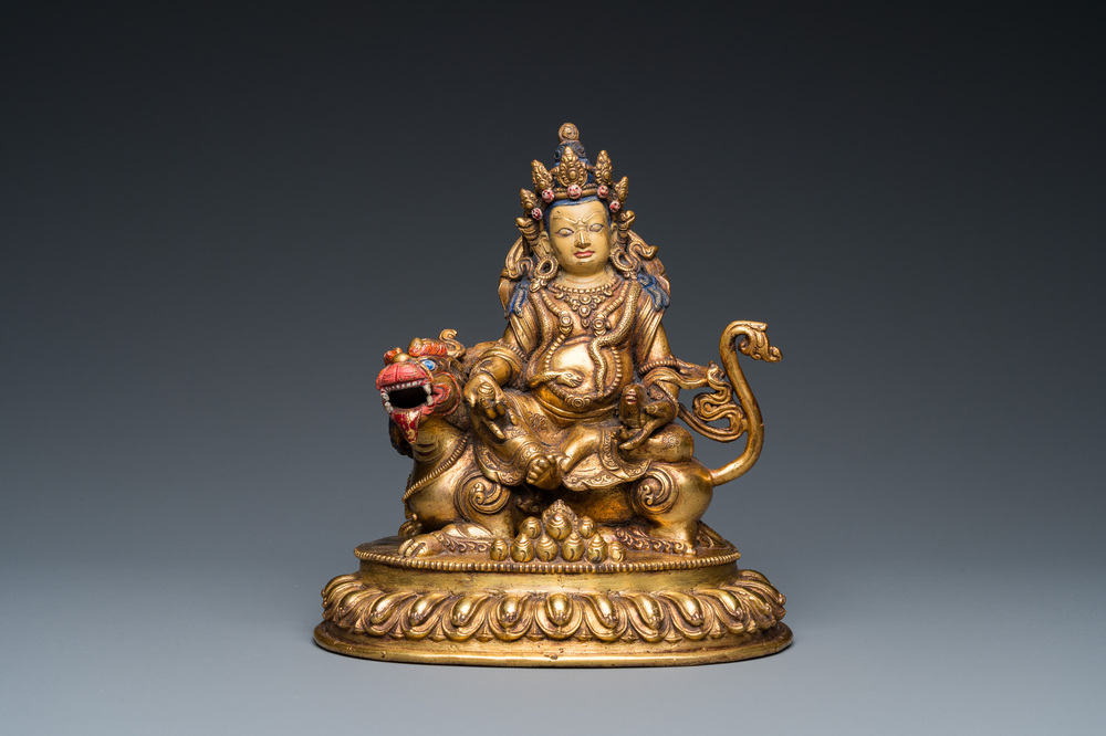 A Tibetan gilt bronze group of Jambhala on his lion, 19/20th C.