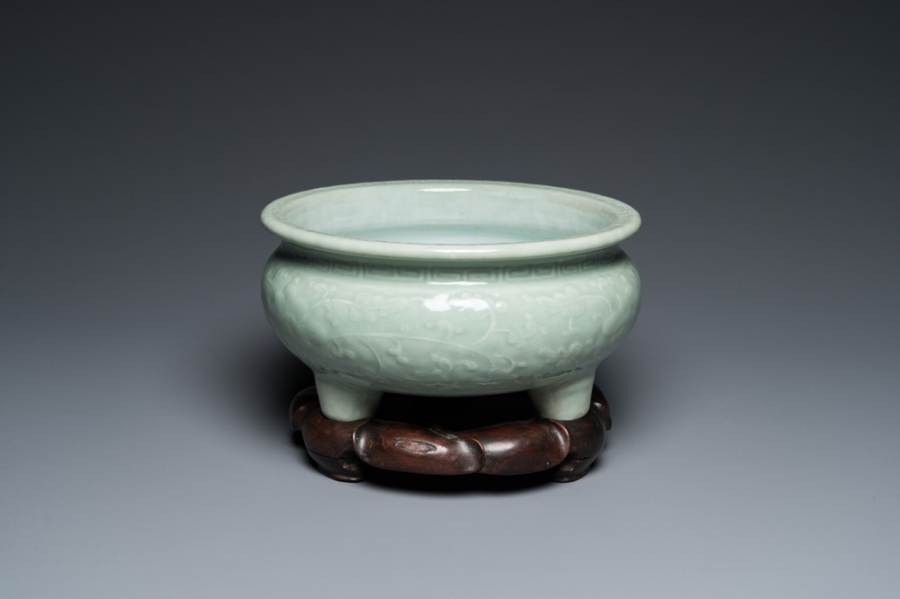 A Chinese celadon-glazed tripod censer with floral scrolls on wooden stand, Qing