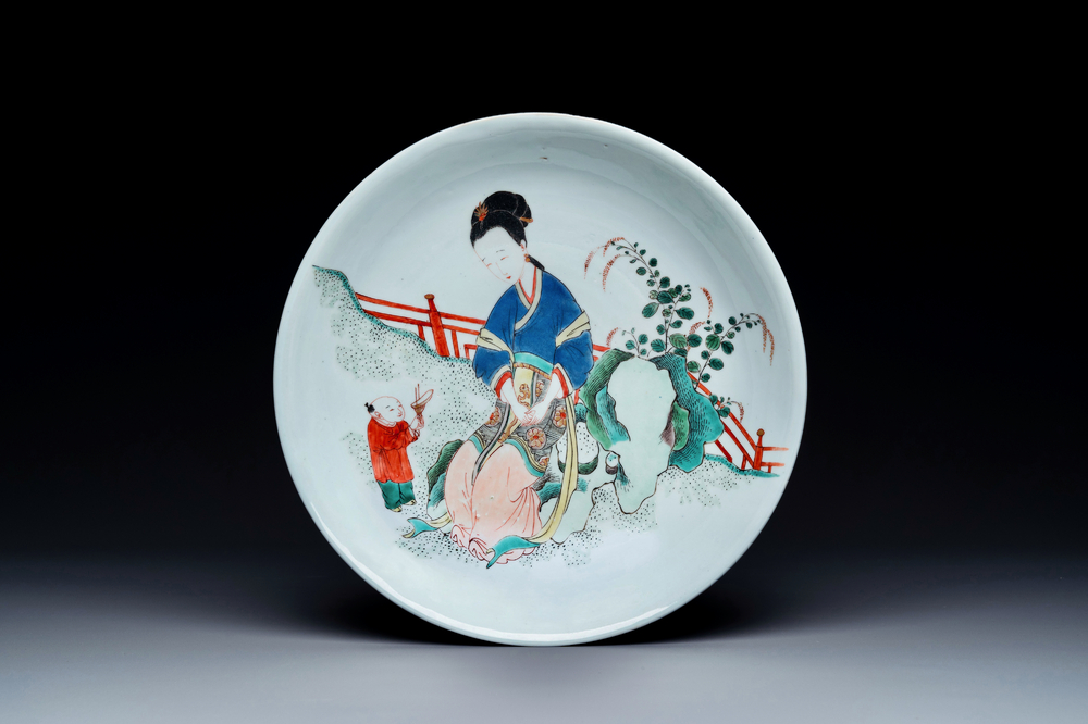 A Chinese famille verte dish with a lady in a garden and a boy offering her a 'jue' vessel, Kangxi