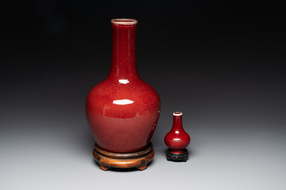 Two Chinese monochrome copper-red-glazed bottle vases on wooden stands, 19th C.
