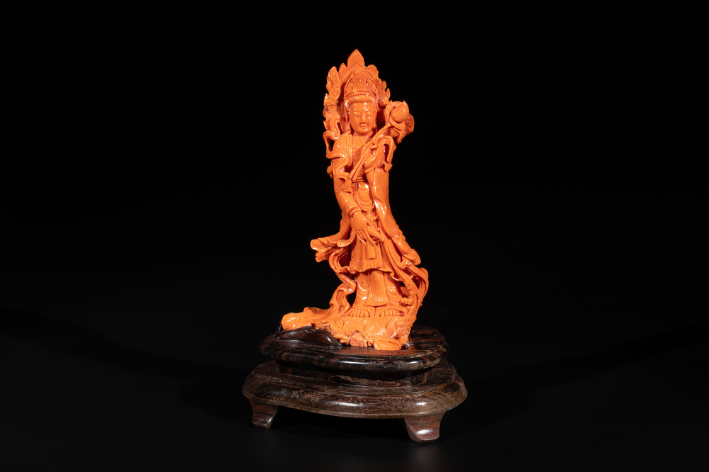 A Chinese red coral Guanyin holding a lotus on wooden stand, 19/20th C.