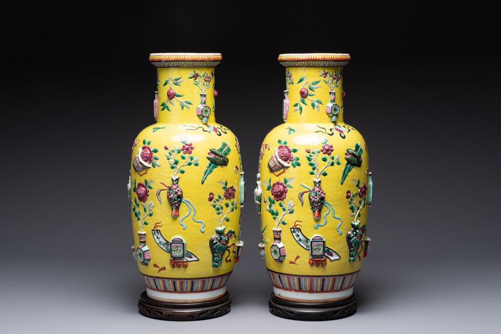 A pair of Chinese famille rose yellow-ground relief-decorated vases with wooden stands, 19th C.