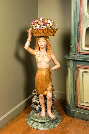 Een polychrome terracotta 'Egyptomanie' sculptuur van een Egyptische dame met bloemenmand, onleesb. gesign., gedat. 1881